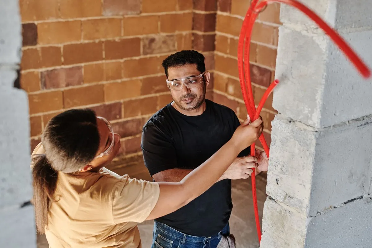 Tradespeople running red water pipe through a brick wall
